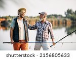 Happy senior fisherman and his son having fun while talking by the lake.  