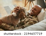 Small photo of Young happy African American veteran cuddling his dog while relaxing on the sofa.