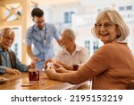 Happy mature woman enjoying in playing card with her friends on patio at residential care home.