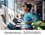 Happy African American athlete jogging on treadmill during her sports training in a gym.