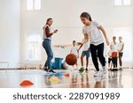 Small photo of Elementary student leading a basketball during physical activity class at school gym. Her coach and friends are int he background.