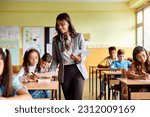 Small photo of Happy Hispanic teacher giving exam paper to her student during a class at primary school.