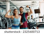 Happy athletic couple flexing their muscles after working out in a gym and looking at camera.