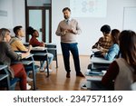 Small photo of University professor talking to group of students during class in lecture hall.