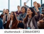 Happy businesswoman raising hand to ask a question attending a seminar in conference hall.