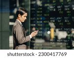 Small photo of Businessman investors in their 30s who check the news with a smartphone in front of the electronic bulletin board reflected on the outdoor stock board