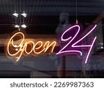 Glowing ad is OPEN 24 hours a day in cafeteria window. Modern electric signboard to attract attention of passers-by. Dark interior and colorful illuminated sign.
