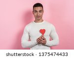 Small photo of Young pretty man holding a heart-object and embosom it, learned to his chest