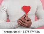 Small photo of Closeup male hands holding a red heart-object and embosom it, learned to chest