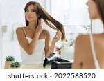 Small photo of Waist up portrait of the woman reflected in mirror doing daily routine while holding hairbrush tidy her hair. Female looking and tangled hair. Beauty treatment concept