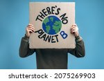 Unrecognizable man holding carton placard with Theres no planet B and hiding his face behind it in front of the camera. Concept of eco activism