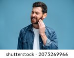 Small photo of Dental problems. Portrait of unhealthy man pressing sore cheek, suffering acute toothache, periodontal disease, cavities or jaw pain. Indoor studio shot isolated on blue background