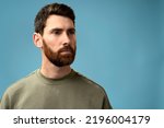 Small photo of Portrait of attentive self confident bearded man looking away with serious expression, unsmiling determined business man. Indoor studio shot isolated on blue background