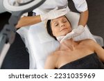 Top view of the pleasant beauty procedure with soft face massage performed by the professional therapist. Mature female laying with closed eyes 