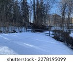 Short wooden fence in the snow.Naked trees and bushes around,houses and blue sky in the background.