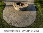 Small photo of round stone fire pit on stamped concrete patio in grass yard