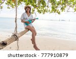 An Asian girl sits on a swing at the beach with an instrumental. Ukulele is a classic song, dressed in a solitary white outfit and reminiscent of a lover far away in summer.