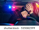 Upset male driver is caught driving under alcohol influence. Man covering his face from police car light.