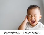 Little toddler boy has earache when insects inside isolated on grey background.2.6 years old baby boy hands touching in ear and screaming.