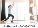 Small photo of Video streaming Stay home.home fitness workout class live streaming online.Asian woman doing strength training cardio aerobic dance exercises watching videos on a smart tv in the living room at home.
