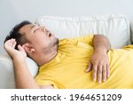 Small photo of Asian man take a nap on sofa with snore.take nap daydreaming in living rooms snoring.Healthcare medical.Sleep health.man sleep at home.Dream, rest, tired father dad day.Sleep Apnea.Sdb.resting at home