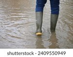 Small photo of Walking through floods in green wellies. Flooded path. Walking through puddle. Wellington boots.