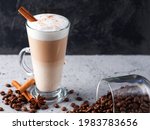 Layered latte coffee on the table in a tall glass. Roasted coffee beans, cinnamon sticks