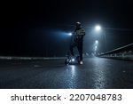 A man rider on an electric scooter is standing on the road, a foggy autumn night, the light from the lanterns