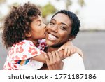 Happy young mother having fun with her child in summer day - Daughter kissing her mum outdoor - Family lifestyle, motherhood, love and tender moments concept - Focus on woman face