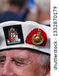Small photo of Plymouth Devon November. White beret worn by veteran solider with two regimental cap badges thereon in close up. One cloth and one gold coloured. View of eyes and nose only.