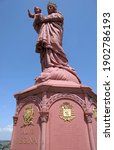Small photo of le Puy en Velay France May 2019.Close up unobstructed view of the pink statue of de Notre Dame de France with the Virgin holding baby Jesus in her right arm. baby is waving. Surrounded by blue sky.