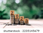 close up stack of coin and 2023 wooden text block on wood table, saving and manage money for new year, e-commerce and shopping online technology, economic crisis risk and problem concept
