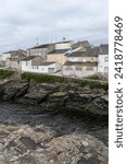 Small photo of town with old, clustered buildings on rocky shores under a cloudy sky, exuding a serene yet somber atmosphere