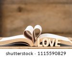 pages of a book curved into a heart shape and word love made by wooden alphabets on wooden table with blurred background