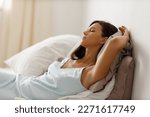 Small photo of Beautiful slender young woman, dressed in gently light blue silk nightie negligee, lies in cozy bed in the bedroom. Attractive girl sleep. Good morning.