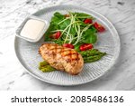 Whole grilled chicken breast, asparagus and tomato salad with arugula in a festive plate on a marble background. Restaurant banquet menu.