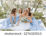 The bridesmaids are in blue dresses, the bride is holding a beautiful bouquet. Sitting enjoying the celebration. Beautiful luxury wedding blog concept. Spring wedding.