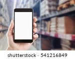 left hand using smartphone with blank screen on Abstract blur background of inside of warehouse with aisle pallet on high shelf