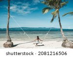 Woman in blue skirt and white top swinging at tropical beach in Thailand
