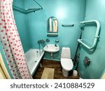 Small photo of The interior of a small, modest bathroom with a bath and a toilet. Green walls, curtains with red dot. The concept of poverty and conciseness