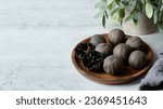 Small photo of black dry persian lime loomi amani in wood plate on white table background. black dry persian lime loomi amani on white table. black dry persian lime loomi amani on white food table background.