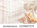 Small photo of Summer minimal flatlay with wide-brimmed hat, colored wine glass, orange fruits in mesh bag on stripes beach towel as background, sun shadows. Summer pastel colored aesthetic photo, copy space