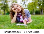 Beautiful dreamy teen girl lying on grass in park with pen and notebook