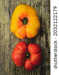 Small photo of Above view of one yellow heirloom tomato and one red heirloom tomato on rustic wood tabletop