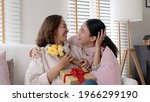 Small photo of Attractive beautiful asian middle age mum sit with grown up daughter give gift box and flower in family moment celebrate mother day. Overjoy bonding cheerful kid embrace relationship with retired mom.