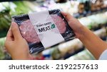 Small photo of Close-up hand carry choose zero pork soy bean faux peas cutlet gluten free read beyond non-meat lab label. Buy raw fake beef tray in asia store veggie burger patty for health care eat diet meal cook.