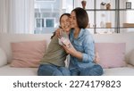 Small photo of May Mother's day young adult grown up child cuddle hug give flower gift box red heart card to mature middle aged mum. Love kiss care mom asia people sitting at home sofa happy smile enjoy family time.