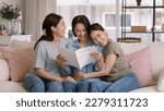 Small photo of Buy mediclaim health care life insure for older mum. Young adult woman asia people grown up child give gift to middle aged mom reading protect cover saving plan paper smile laugh sitting at sofa home.