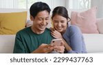 Small photo of Asia people young family man woman smile happy fun laugh look at phone sit at home pay for hotel booking, search choose, buy ticket on social media app for budget travel abroad trip getaway plan tour.