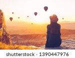 Small photo of A woman alone unplugged sits on top of a mountain and admires the flight of hot air balloons in Cappadocia in Turkey. Digital detox and soul search